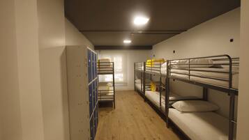 A dormitory room with bunk beds, a wardrobe, and a window with natural light.