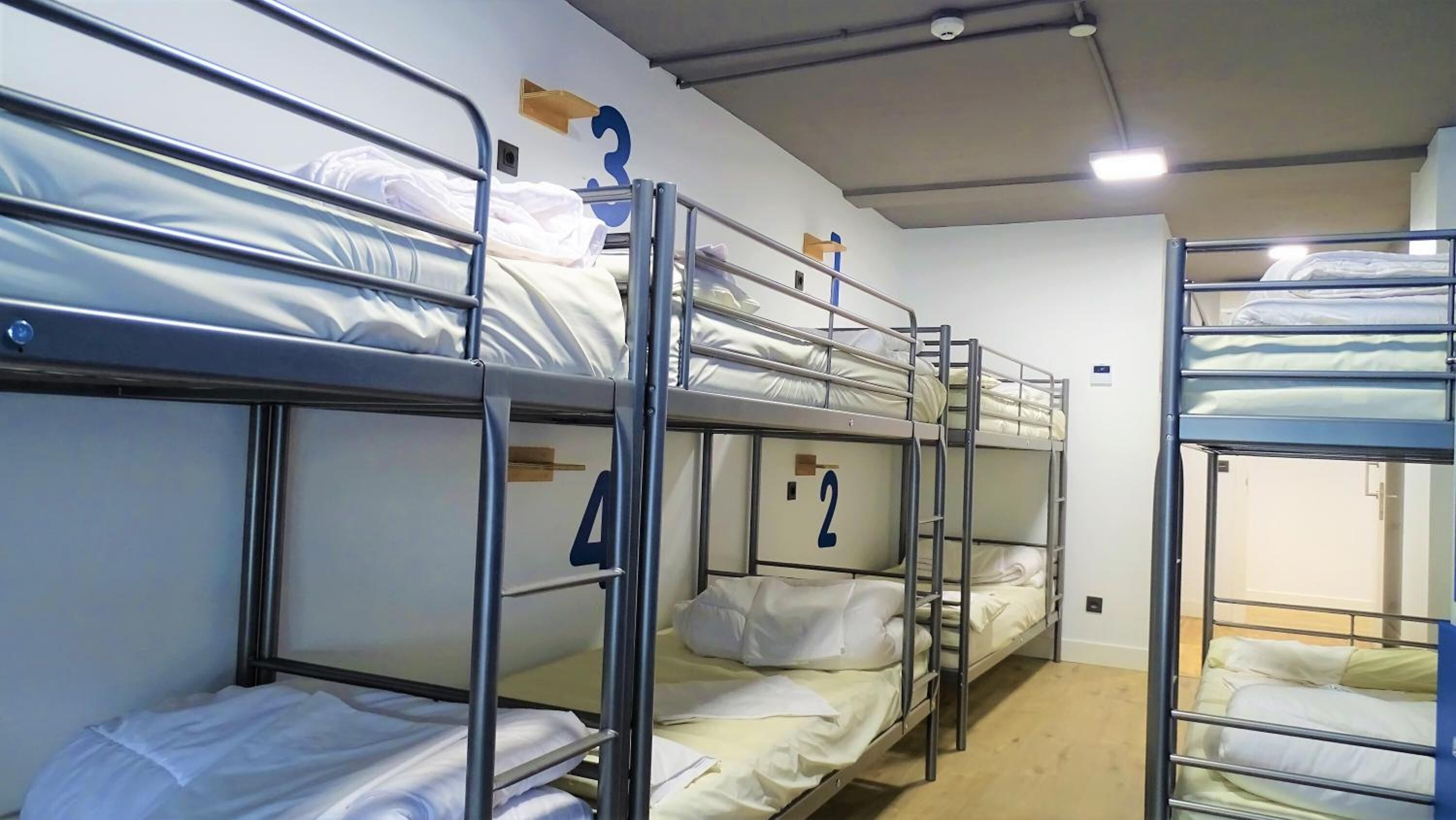 A bunk bed room with metal railings, white bedding, and a visible number '3' on the wall.