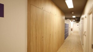Un couloir avec des casiers en bois, un sol carrelé et un plafond doté d’un éclairage encastré.
