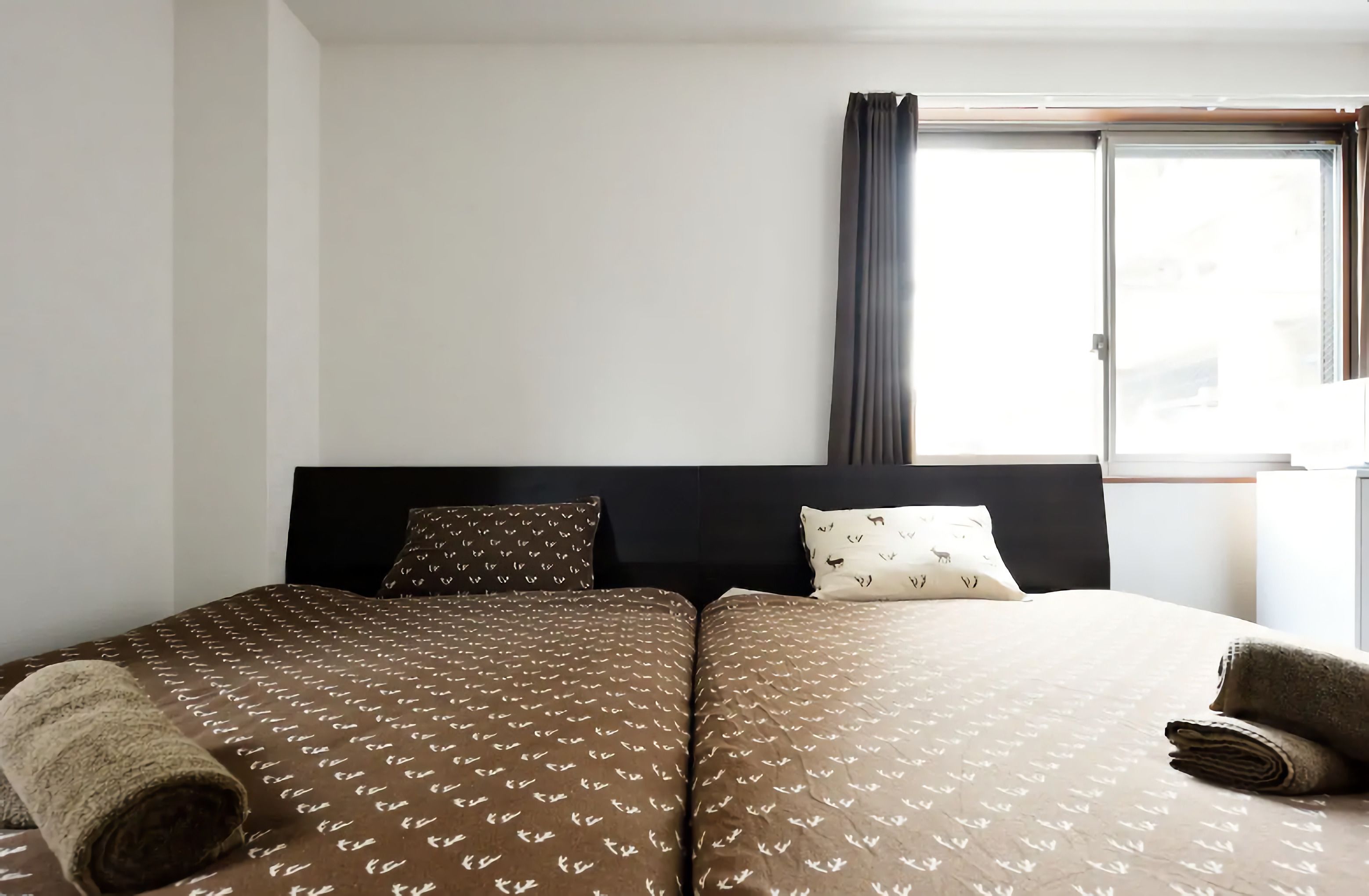 Une chambre d’hôtel avec un lit double, deux oreillers, une fenêtre avec des rideaux et une tête de lit.