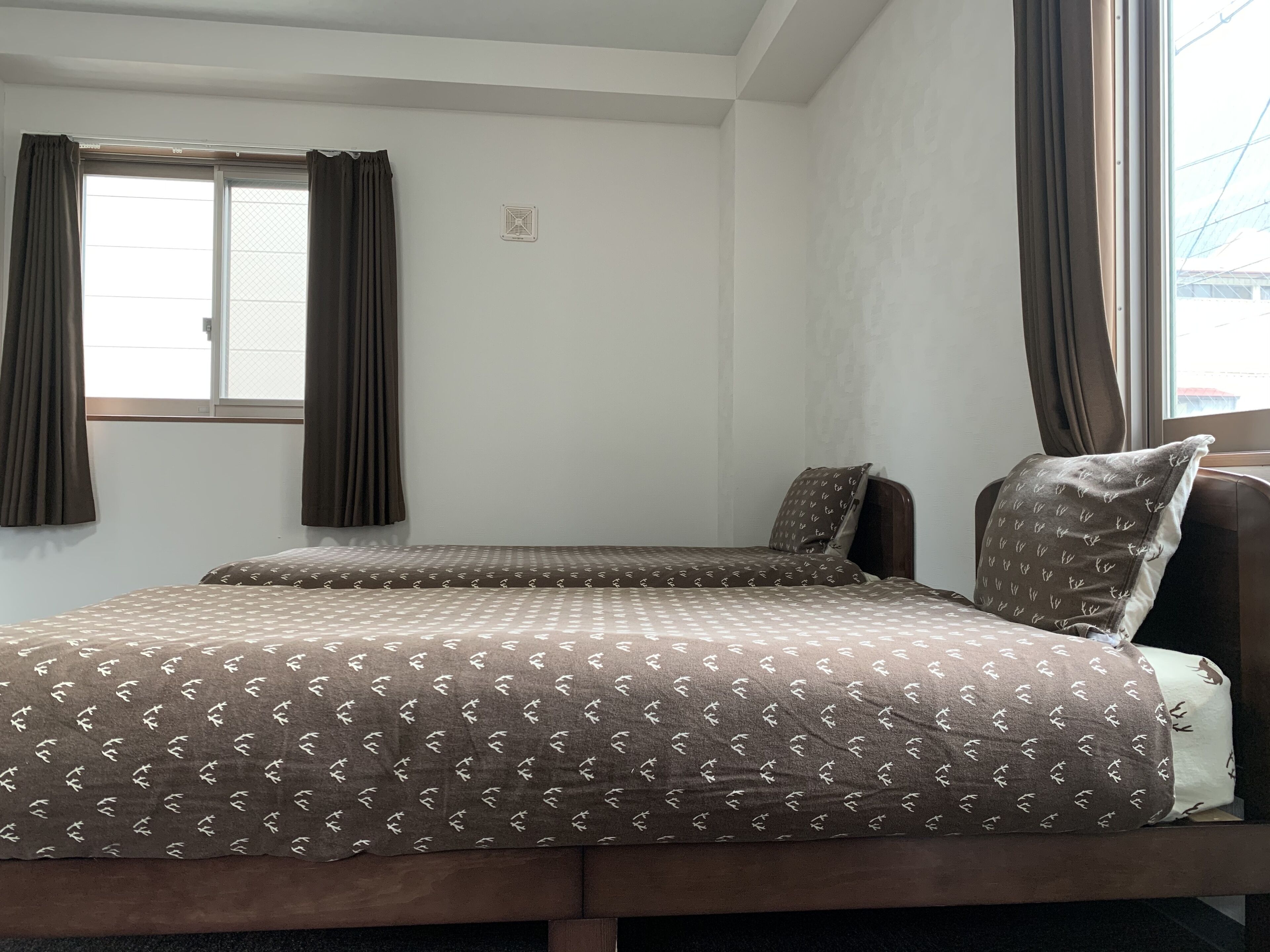 Een kamer met een bed, een raam met gordijnen en een aan de muur bevestigde thermostaat.