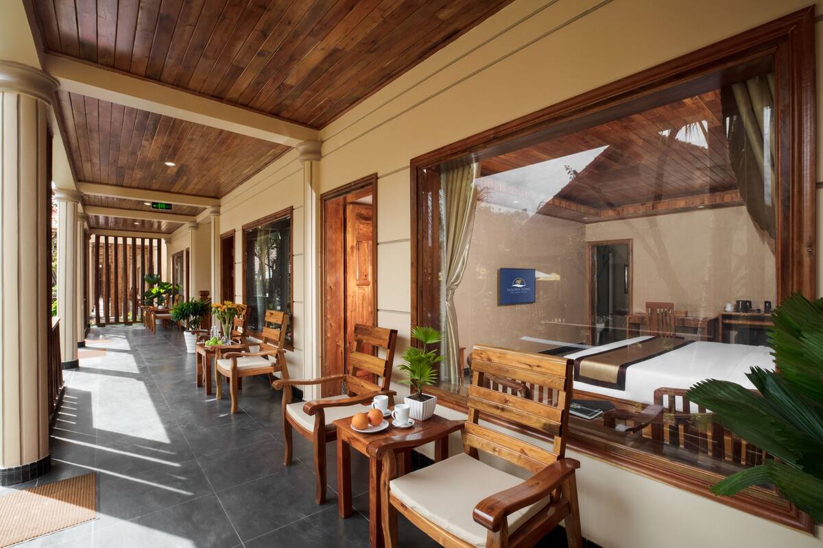 Un couloir avec des chaises et des tables en bois, une plante en pot et une vue à travers de grandes fenêtres.
