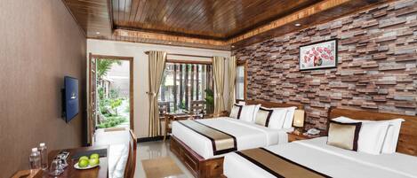 A hotel room with two beds, a wooden ceiling, a brick-patterned wall, a TV, a desk with a chair, and a window with curtains.