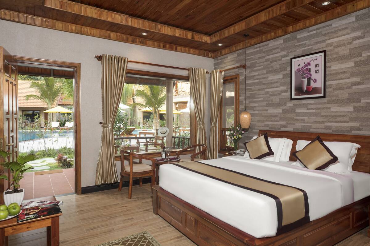 Une chambre spacieuse avec un grand lit, un plafond en bois et une vue sur l’espace piscine.