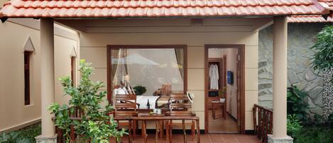 A covered outdoor seating area with a table and chairs, a stone wall, and a tiled roof.