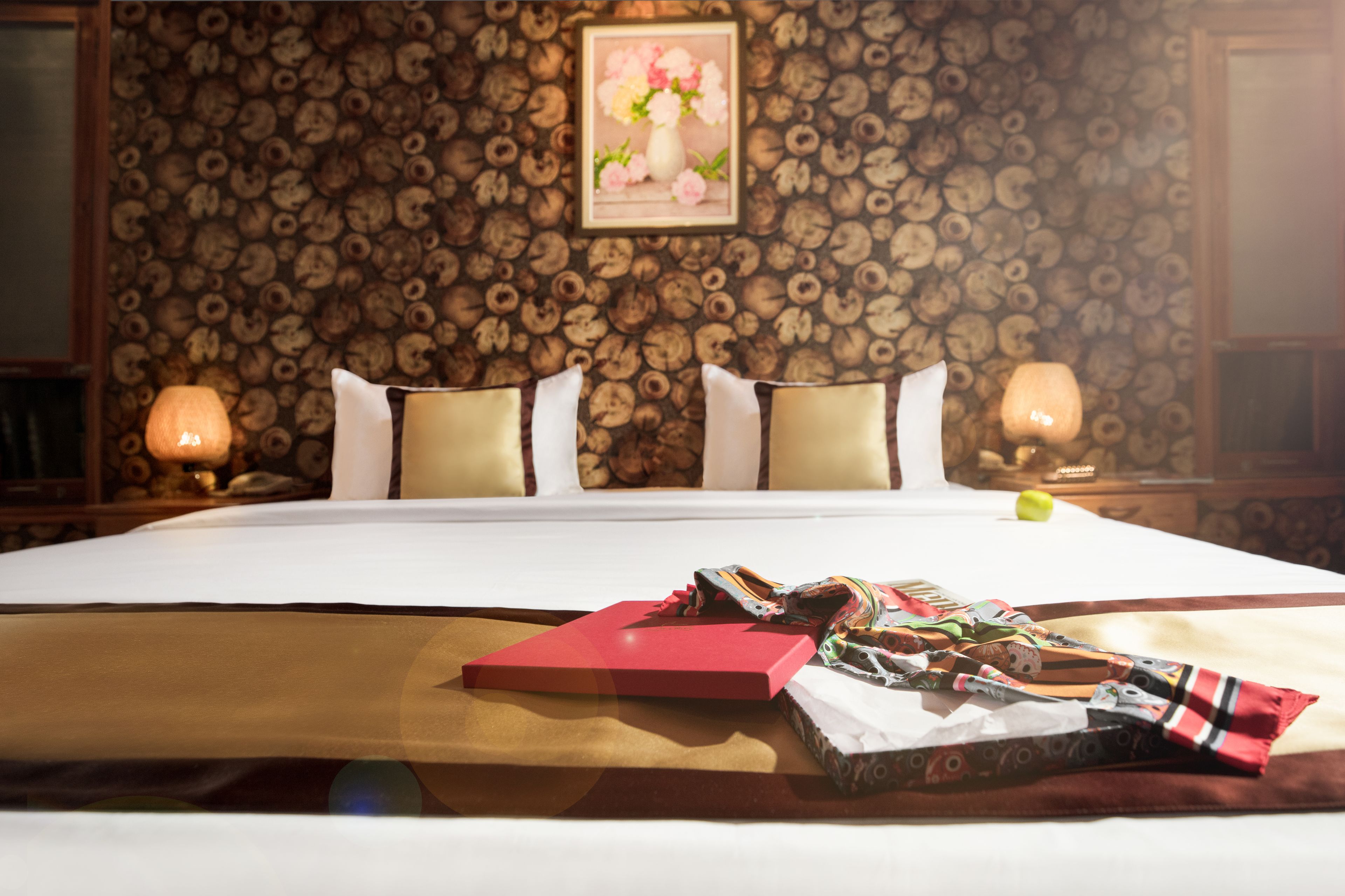 A hotel room with a large bed, two bedside lamps, a framed picture on the wall, and a red folder on the bed.