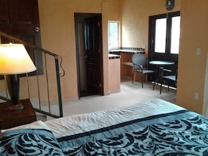 Une chambre à coucher avec un lit, un bureau et une chaise. Il y a une fenêtre et une porte qui donne sur une autre pièce.