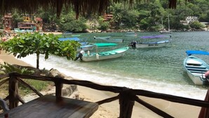 Una playa con varias embarcaciones amarradas, una mesa de madera y una estructura techada de paja.
