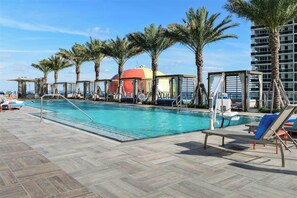 Un área de piscina con sillones reclinables, palmeras y un edificio con cúpula roja.