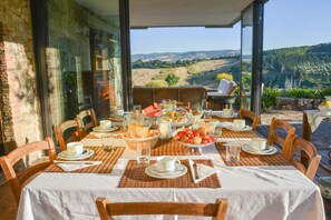 Enjoy breakfast with a scenic view of the countryside from this dining area, featuring a table set with a variety of dishes and beverages.