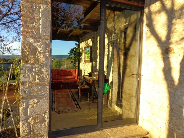 A stone building with a red sofa and a table, a green umbrella, and a view of the landscape. - Agriturismo Fontenuova (Manciano)