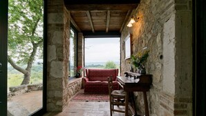 Una habitación rústica con pared de piedra, techo de madera, un sofá rojo con estampado, una mesa de madera y vistas al exterior con vegetación.