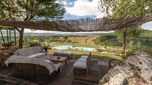 Un área de estar al aire libre con mobiliario de mimbre, una terraza de madera y vistas a una piscina y al paisaje.