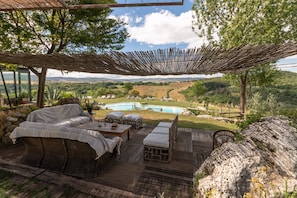 An outdoor seating area with wicker furniture, a wooden deck, and a view of a swimming pool and landscape. - Agriturismo Fontenuova (Manciano)