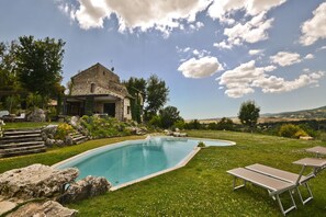 Relax by the serene pool surrounded by lush greenery and a picturesque view of rolling hills.