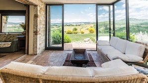 Una habitación iluminada por el sol con un sofá de mimbre, una mesita y vistas a un paisaje exuberante a través de amplios ventanales.