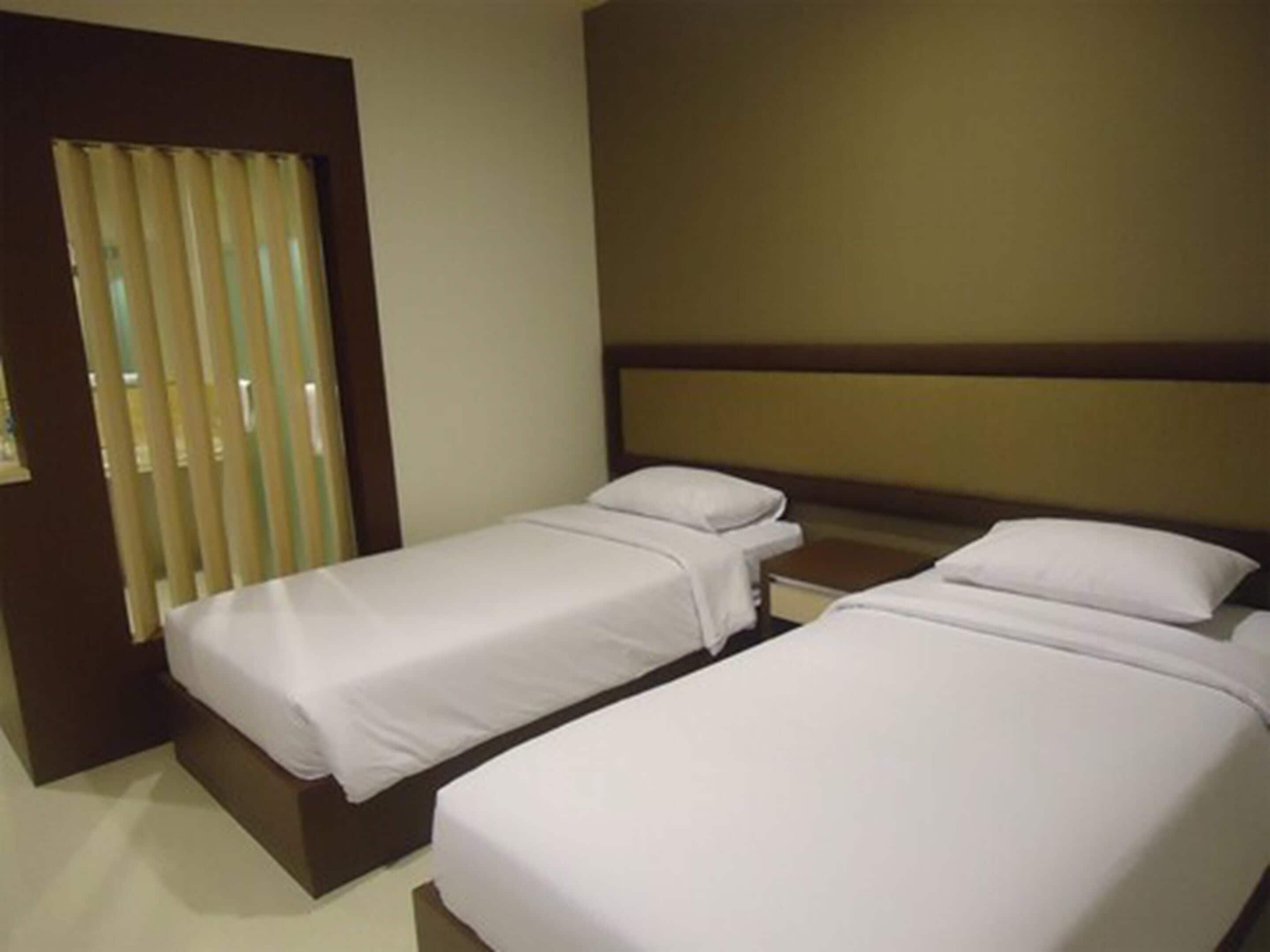 Habitación de hotel con dos camas individuales, cabecero de madera, mesita de noche y ventana con persianas.