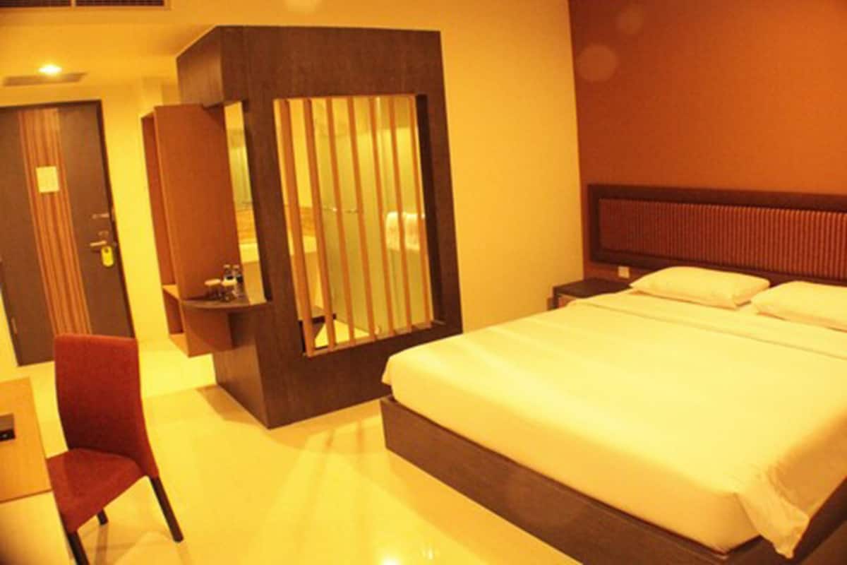 Habitación de hotel con una cama grande, una silla, un escritorio y un espejo.