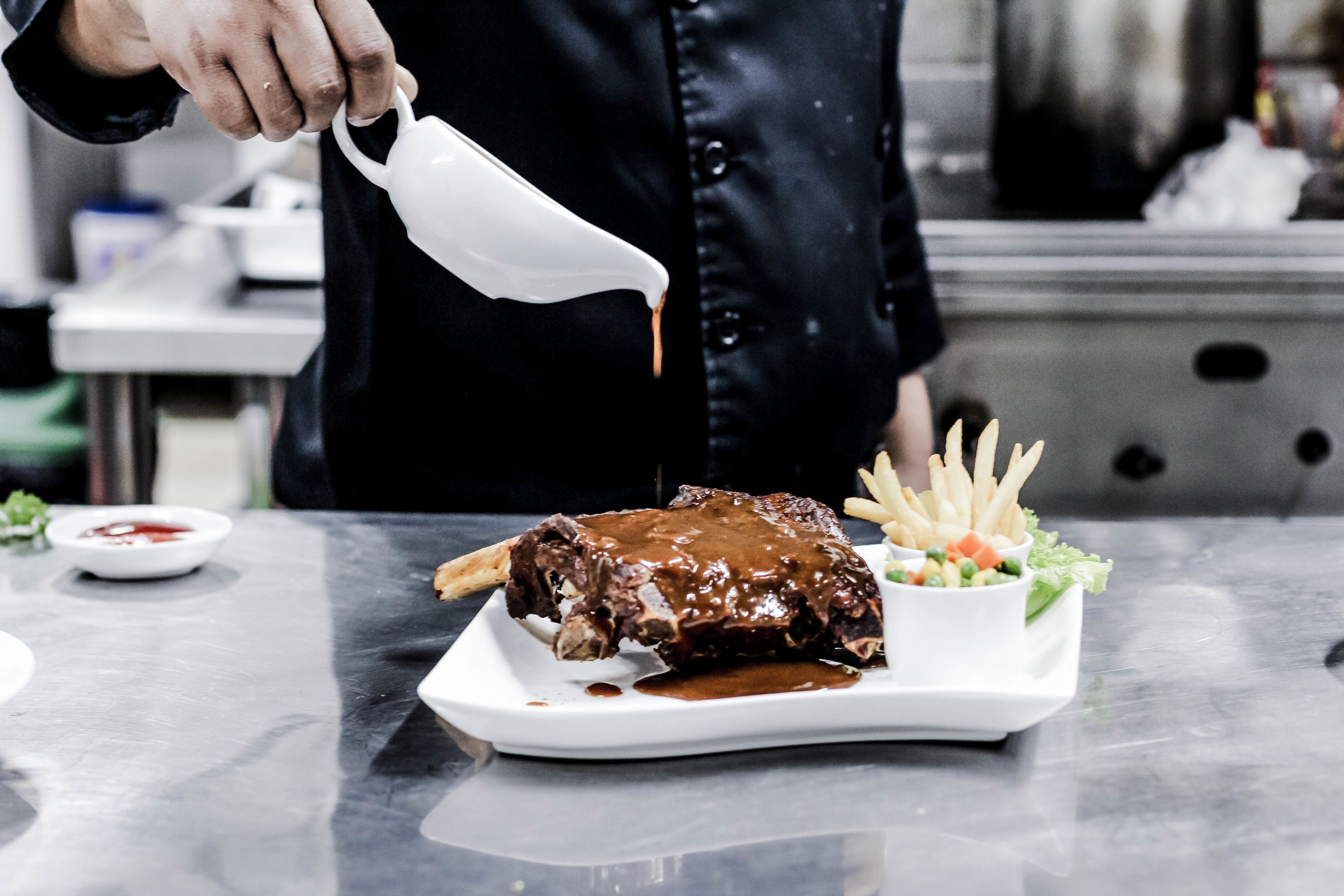 Un chef versant de la sauce sur un plat de viande et de frites.