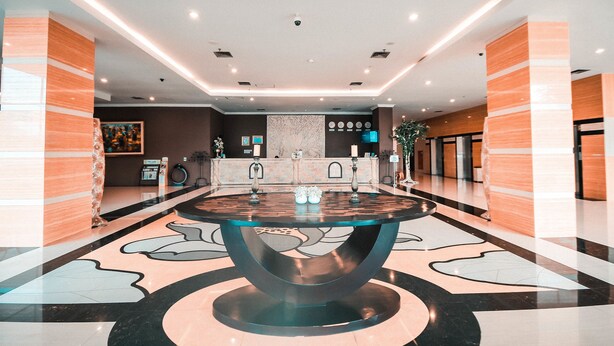 Um lobby moderno com uma mesa redonda central, um balcão de recepção e uma parede decorativa.