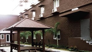 Um pátio com um gazebo de madeira, bancos de pedra e um edifício de tijolos com aparelhos de ar condicionado.