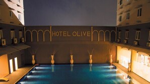 Uma piscina com a inscrição 'HOTEL OLIVE' na água, rodeada por edifícios.