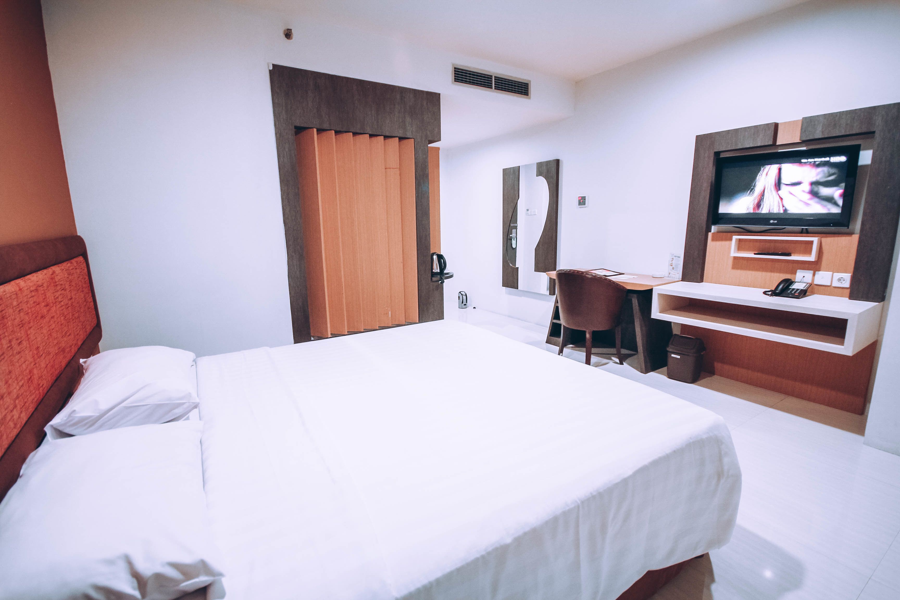 A hotel room with a bed, a desk, a chair, a television, and a mirror.