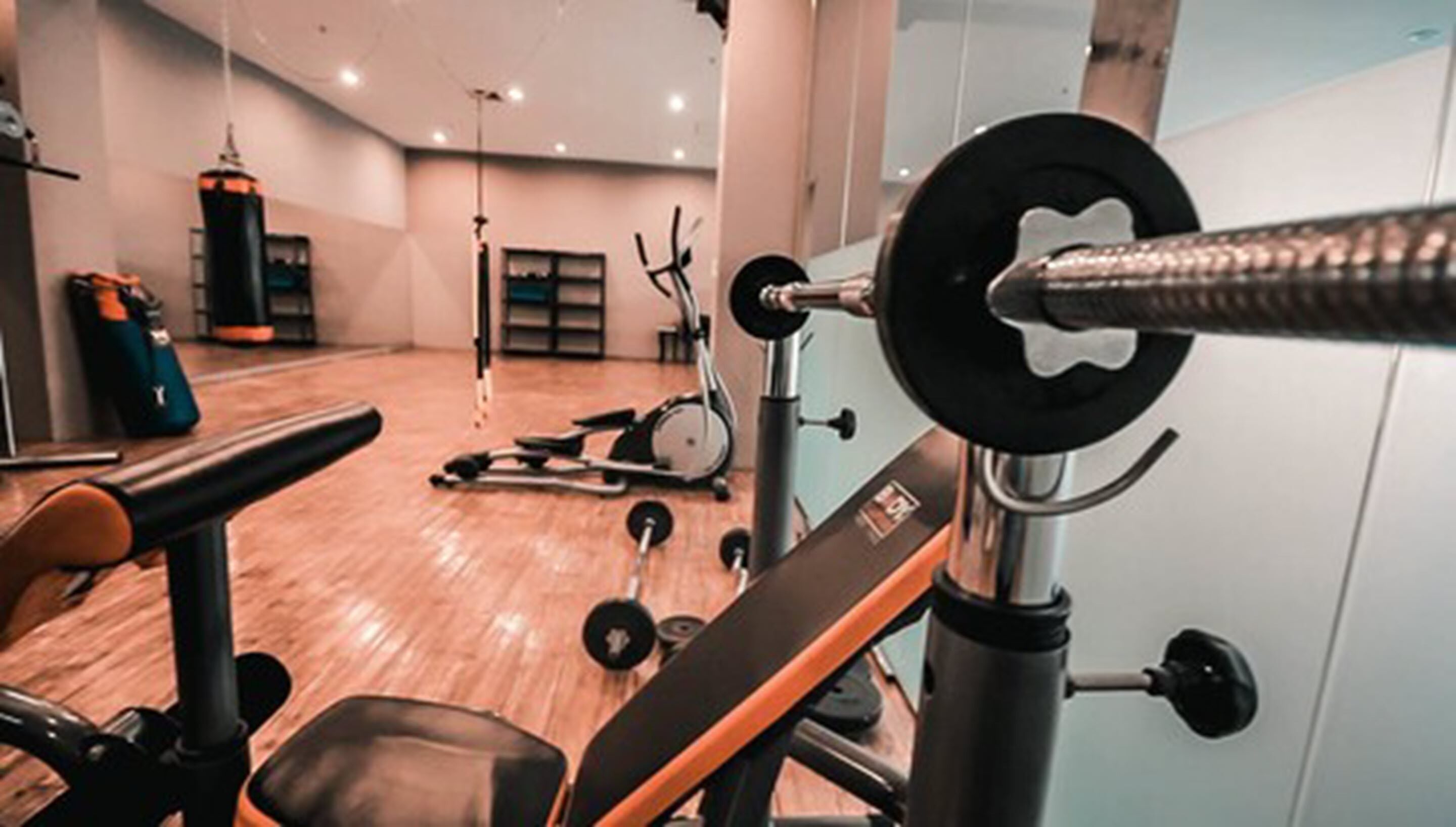 Un gimnasio con equipo de levantamiento de pesas, una banca y máquinas de cardio.