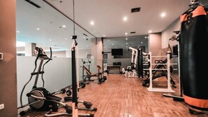 Uma academia com equipamentos de ginástica, um saco de pancadas e uma televisão na parede.