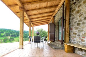 Une terrasse couverte avec des poutres en bois, des murs en pierre et une vue sur la campagne.