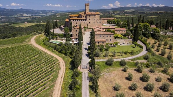 A large castle with a tower, surrounded by vineyards and a well-maintained lawn.