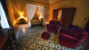 Una habitación con una cama, dos sillones rojos, un armario de madera y un suelo estampado.