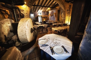 Un comedor rústico con paredes de piedra, vigas de madera y mesas dispuestas para una comida.