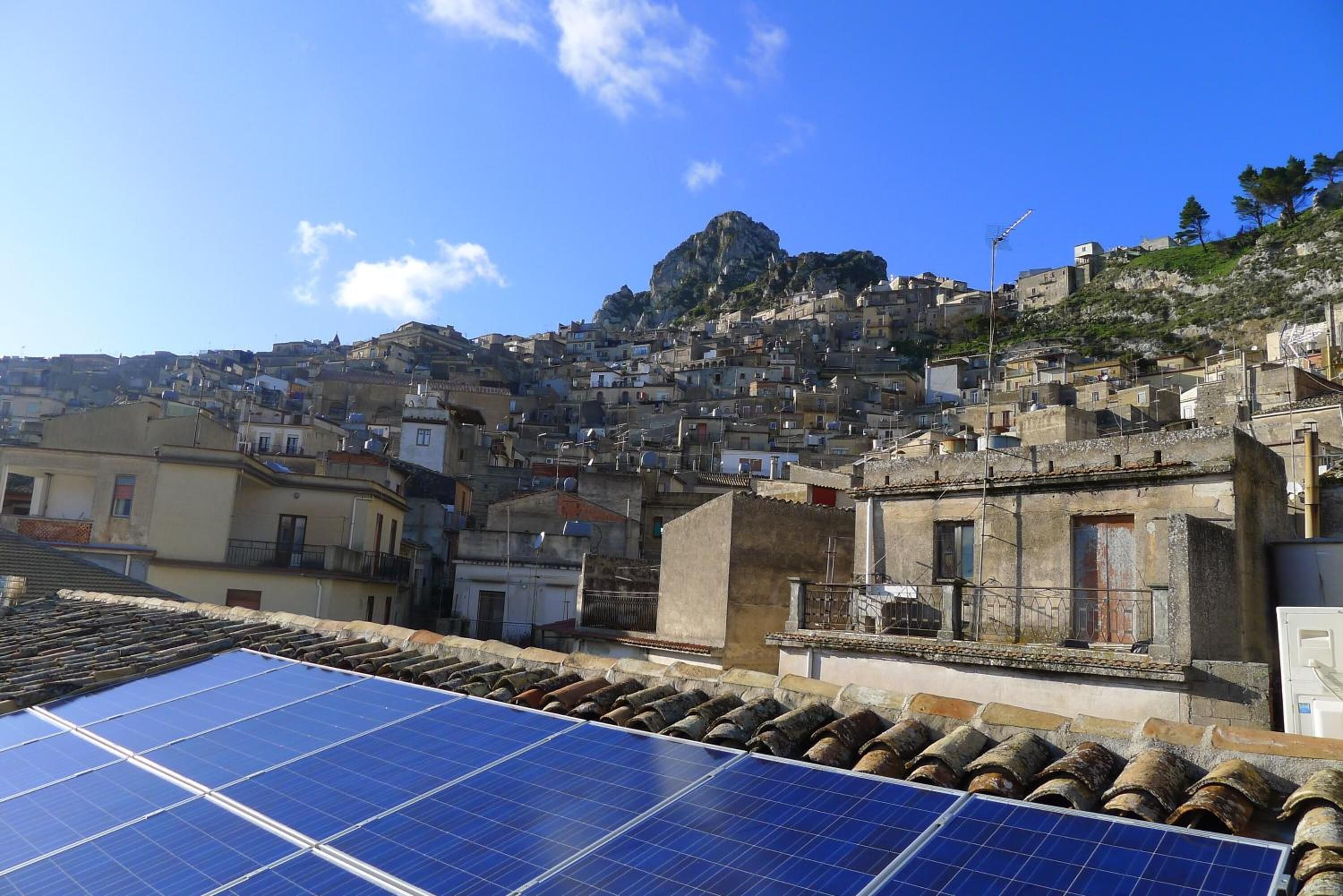 A densely packed hillside town with traditional architecture and a prominent rocky hill in the background.