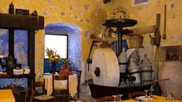 A rustic dining area with a large stone oven, wooden furniture, and a window with a view.