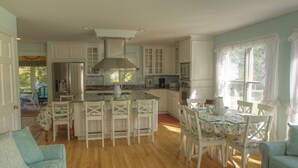 A spacious kitchen with white cabinetry, a central island, and a dining area with white chairs. - Pristine Chappy! August 29 through Labor Day 2026 Available !  (Chappaquiddick Island, Edgartown)