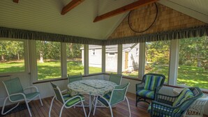 A covered patio with a round table and chairs, large windows, and a view of the yard. - Pristine Chappy! August 29 through Labor Day 2026 Available !  (Chappaquiddick Island, Edgartown)