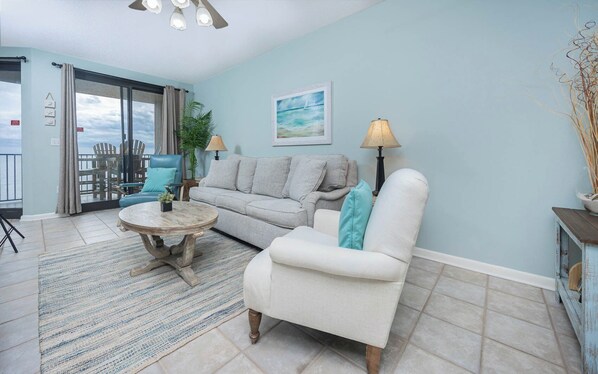 A living room with a sofa, armchair, coffee table, and a painting on the wall. - XTRA HALF BATH ~ Phoenix 10 One Bedroom on the BEACH! (Orange Beach)