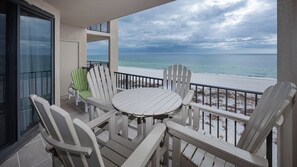 A balcony with a round table and four Adirondack chairs, overlooking a beach with a cloudy sky. - XTRA HALF BATH ~ Phoenix 10 One Bedroom on the BEACH! (Orange Beach)