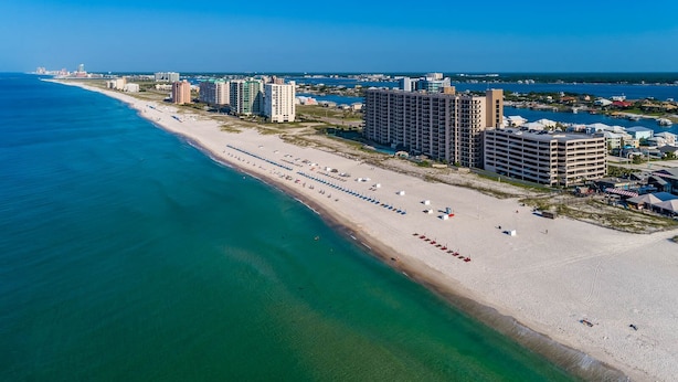 Eine Küstenstadt mit einem langen Sandstrand, Hochhäusern und blauem Himmel.
