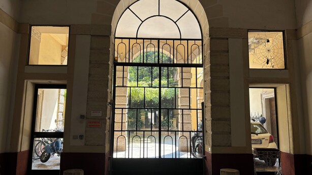 An arched entrance with a metal gate, leading to a courtyard with parked bicycles and a scooter. - Casa Magnolia (Verona)