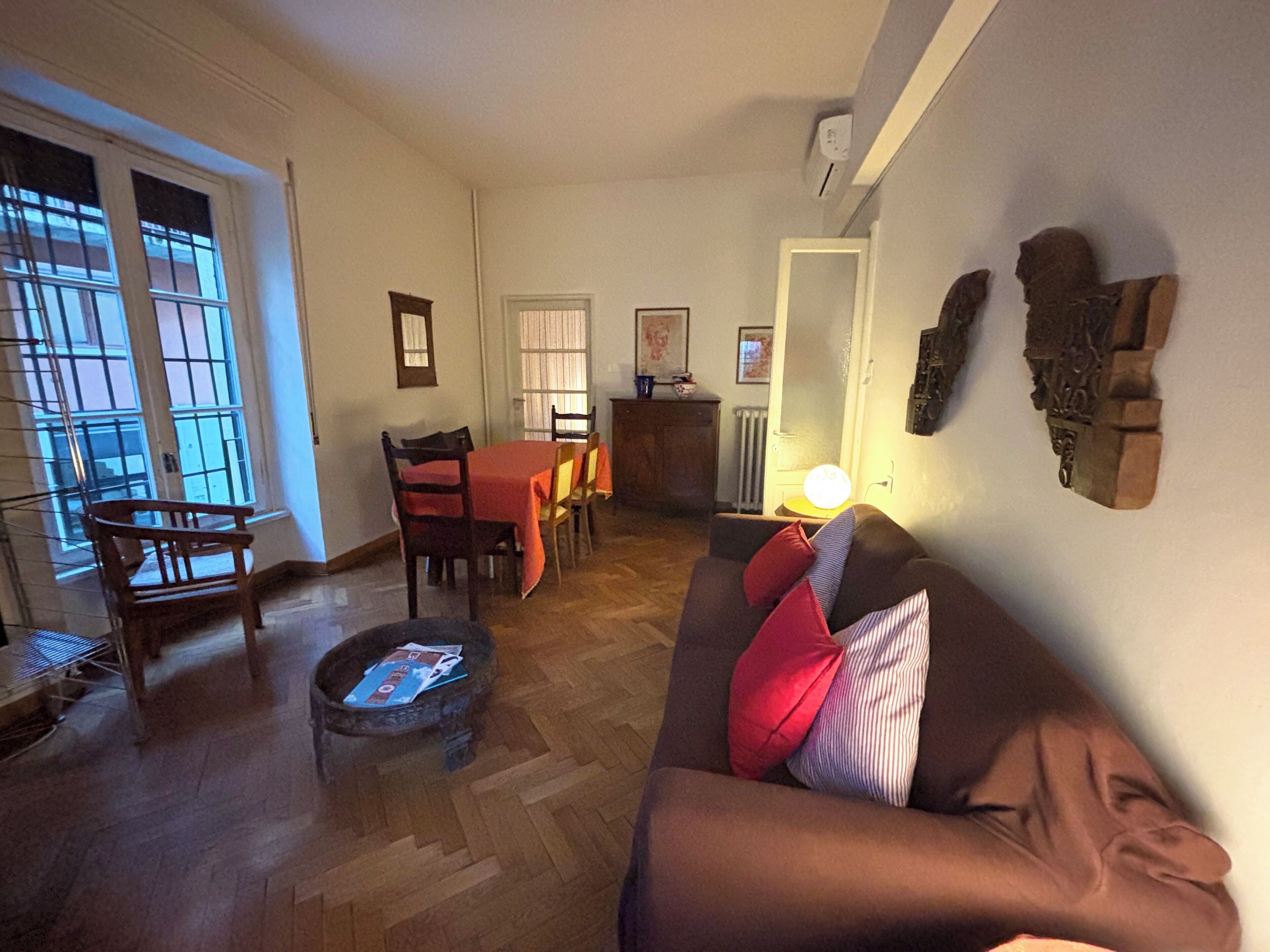 Uma sala de estar com um sofá marrom, cadeiras de madeira, uma mesa de jantar e uma lareira.