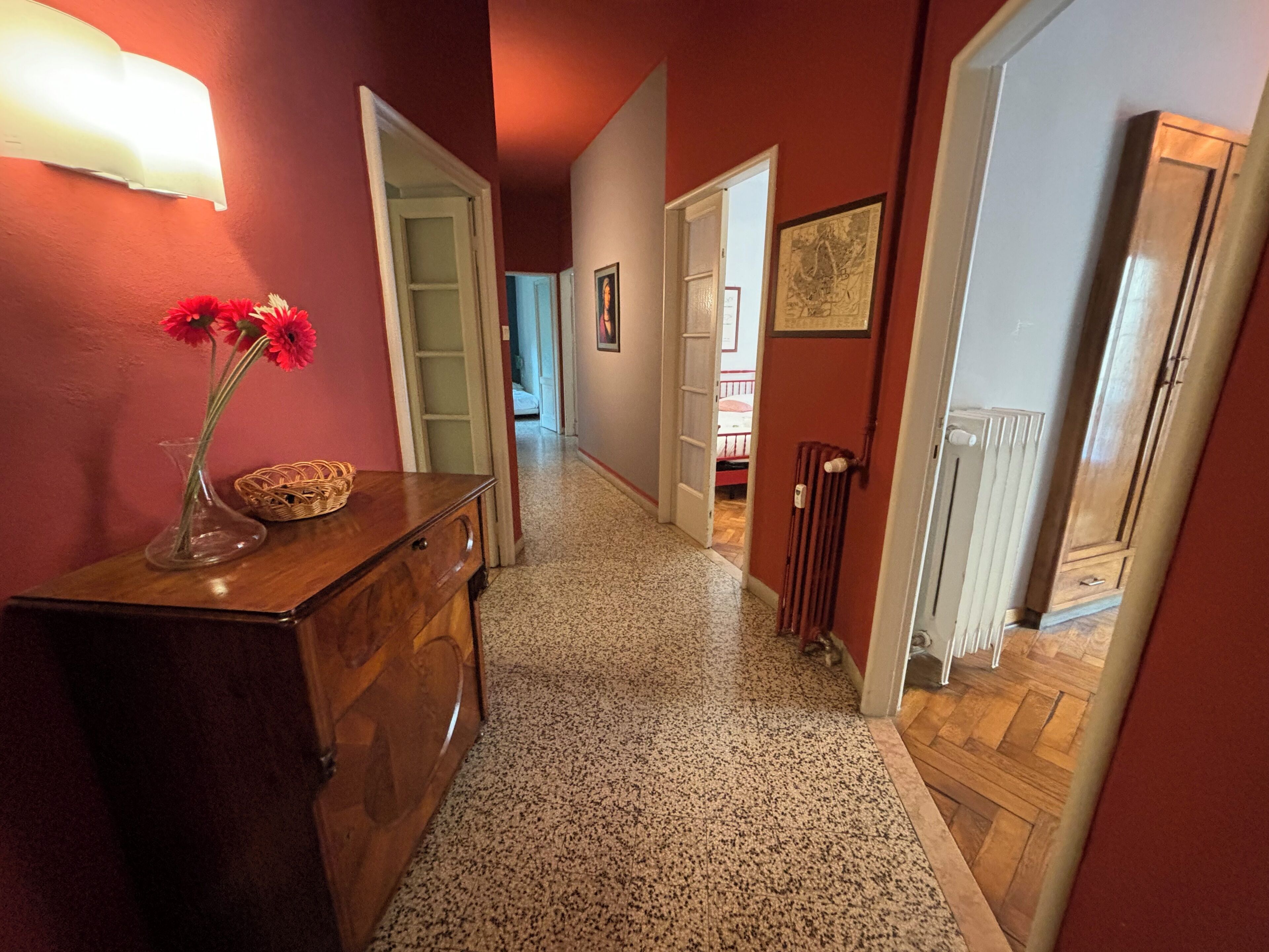 A hallway with a wooden dresser, a vase with flowers, and a framed picture on the wall.