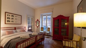 A bedroom with two beds, a red wardrobe, a mirror, and a window with a view. - Casa Magnolia (Verona)