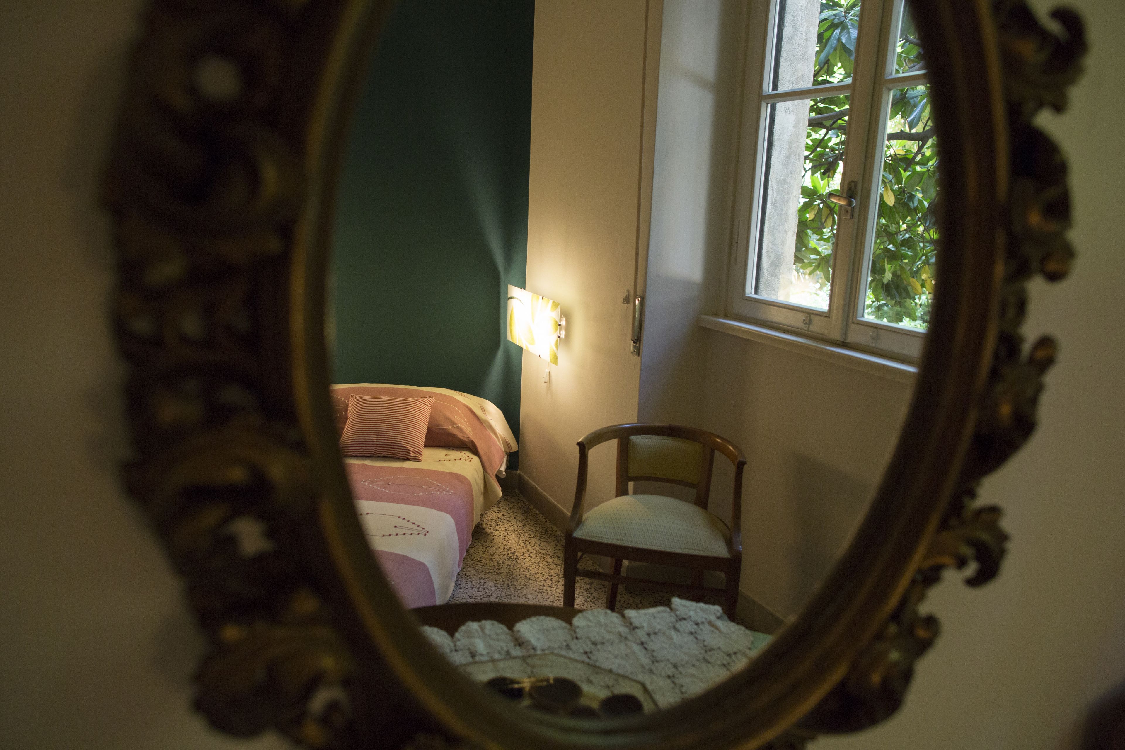 A bedroom with a bed, a chair, and a window with greenery outside.