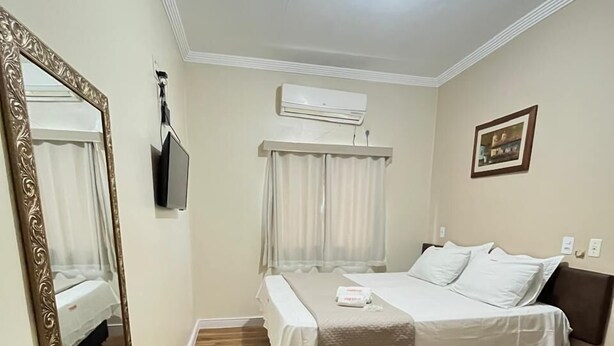 A bedroom with a bed, a mirror, a TV, and an air conditioning unit. - Hotel Marcan (Sumare)