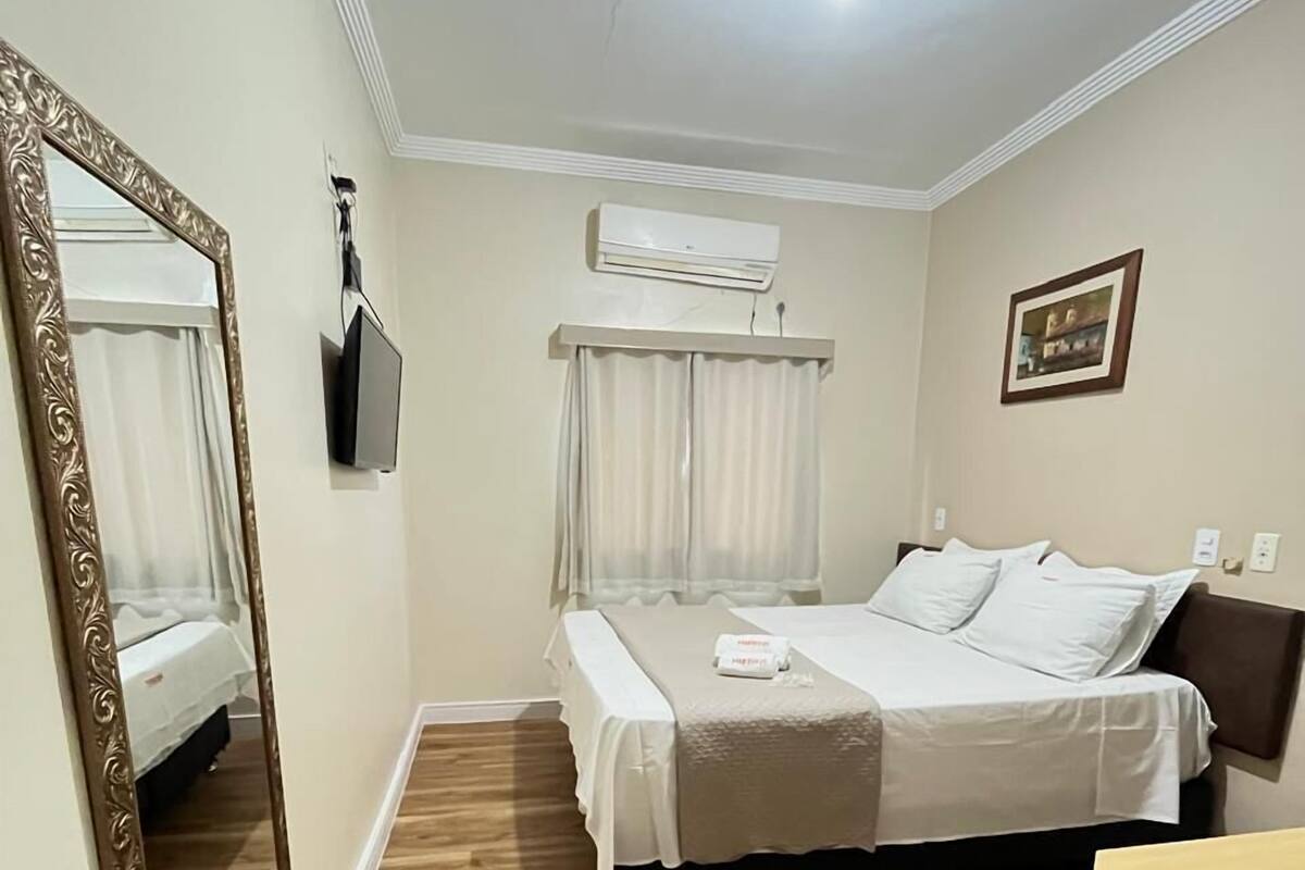 Un dormitorio con cama, espejo, televisión y aire acondicionado.