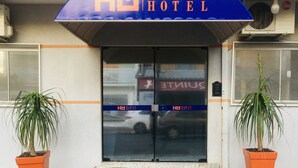 The entrance to the Marcan Hotel with a blue awning and two potted plants. - Hotel Marcan (Sumare)