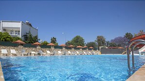 A swimming pool with lounge chairs and umbrellas, a stone wall, and a building in the background. - Mysea Hotels Incekum (Alanya)