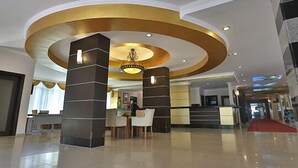 A hotel lobby with a modern design, featuring a central reception desk, a chandelier, and a red carpet leading to the entrance. - Mysea Hotels Incekum (Alanya)